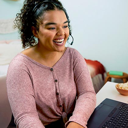 woman with curly hair and headset talking in front of a laptop. 