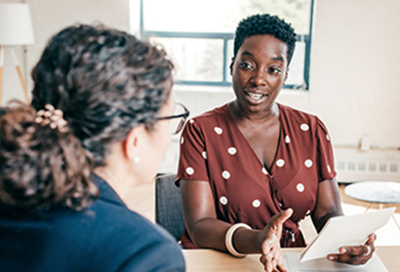 Two women talking in office setting. 