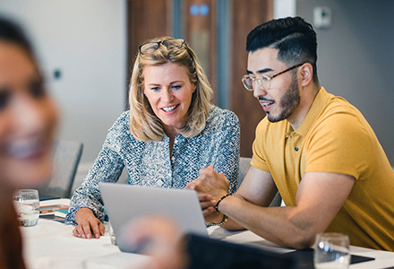 Woman and man in office setting working together on a laptop. 