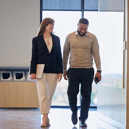 Two employees in business casual clothes walking down a hallway together. 