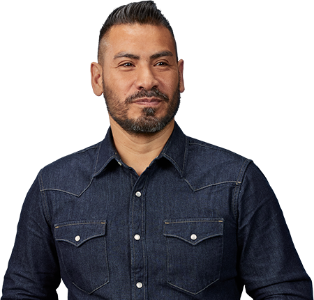 man with dark facial hair wearing button up denim shirt looking into the distance. 
