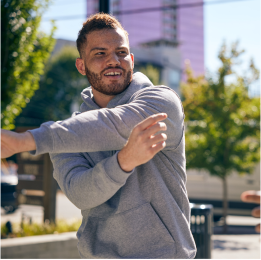 man outside in gray sweatshirt stretching his arm.