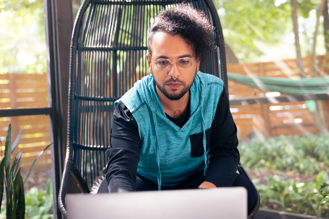 male with glasses and nose ring working on laptop outside. 