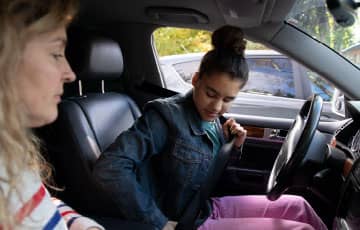 Teen buckling her seatbelt in the driver's seat of a car. 