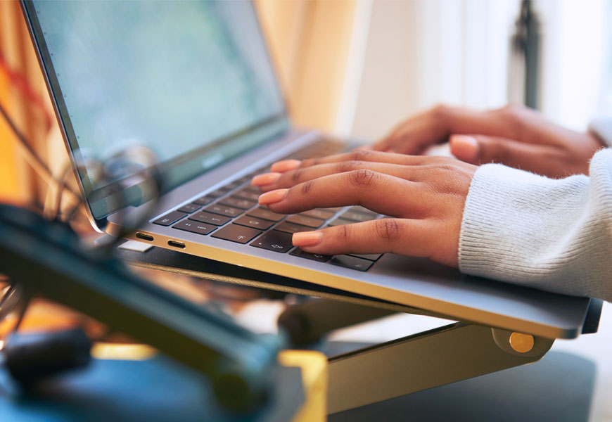 A woman standing next to a window on a laptop computer. 