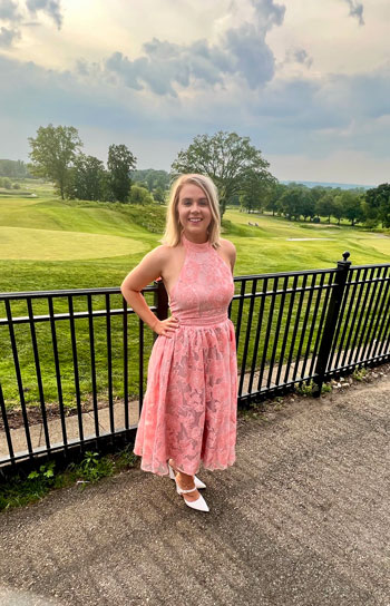 Woman in pink dress standing in front of a golf course. 