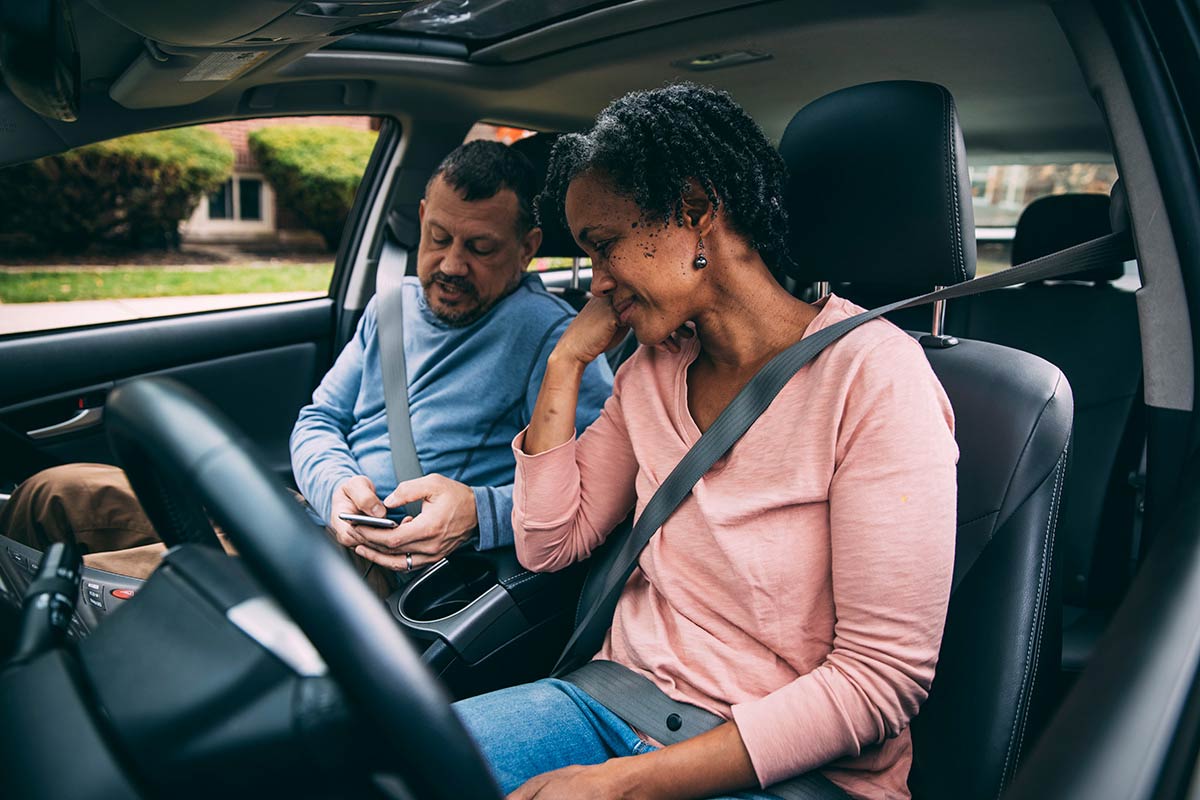 A couple sitting in their car and looking at a phone. 