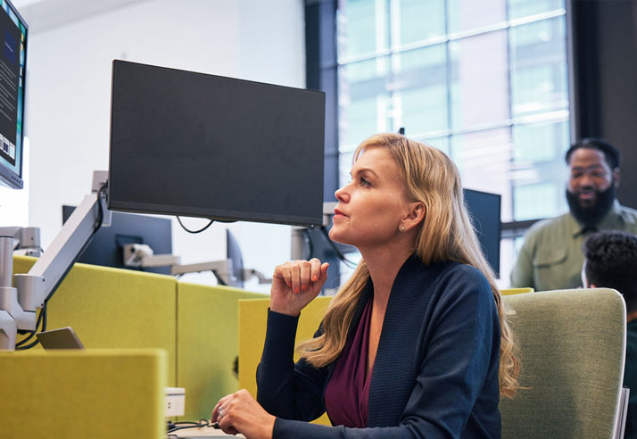 Blonde woman watching a computer screen at a desk. 