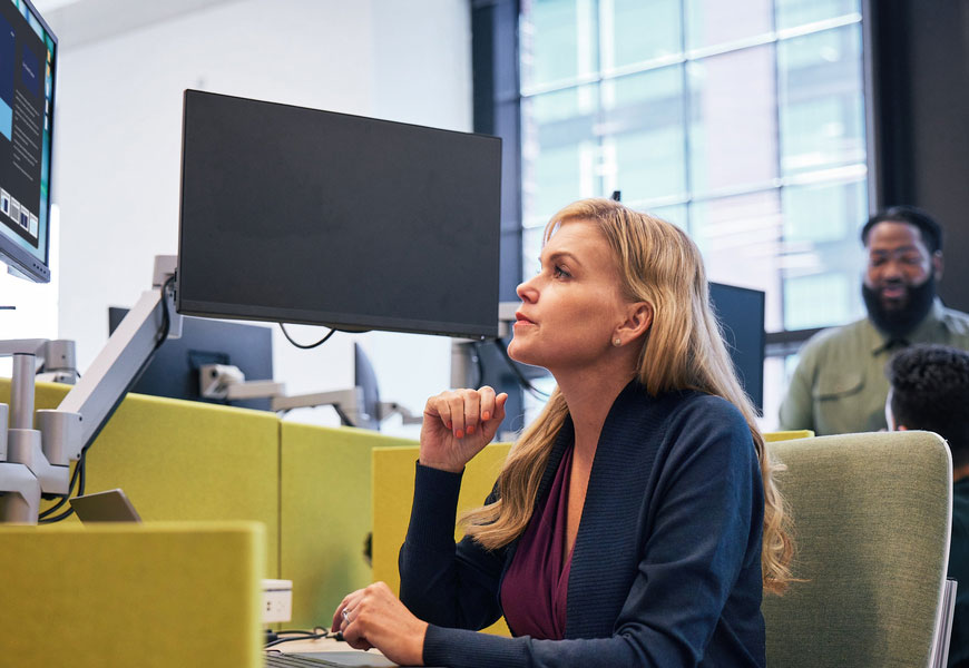Blond woman watching a computer screen at a desk. 
