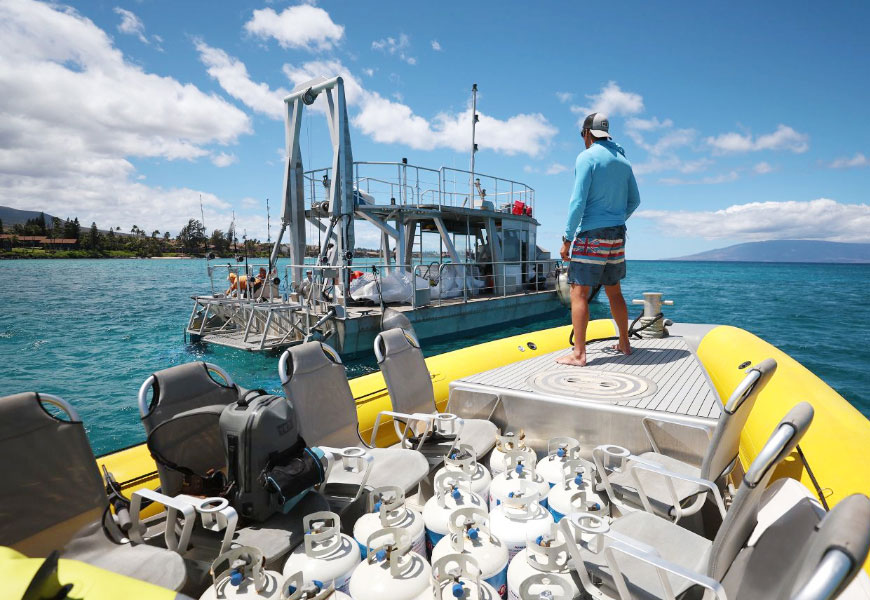 Allstate employee Aaron Goddard standing on bow of a boat with propane tanks behind him. 