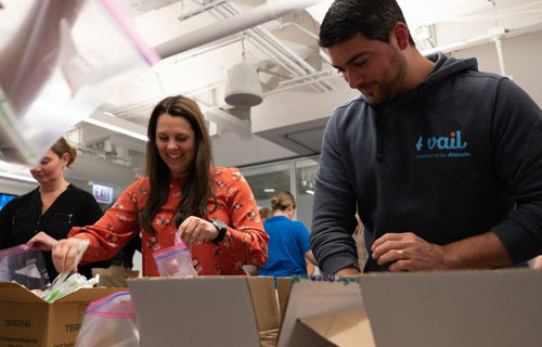 Man with hoodie and woman in orange shirt smiling in front of packing boxes