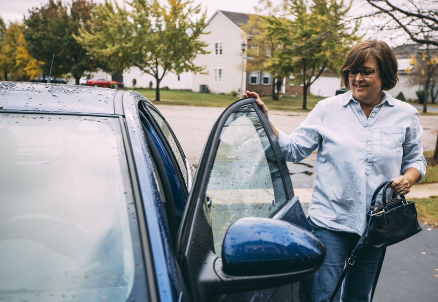Woman smiling standing next to blue car with door open. 