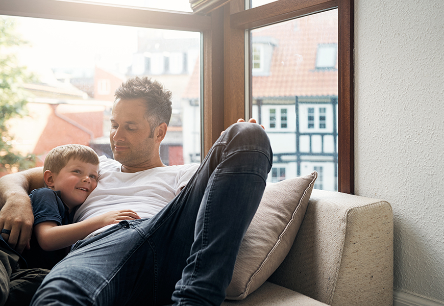 Man sitting with young boy on a couch by a window 